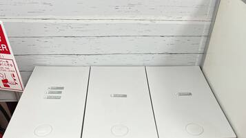 Three white waste bins with recycling symbols, placed against a white wall with a red fire extinguisher to the left.