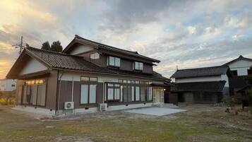 Une maison traditionnelle japonaise, avec un toit recouvert de tuiles, une grande cour ouverte et une zone herbeuse.