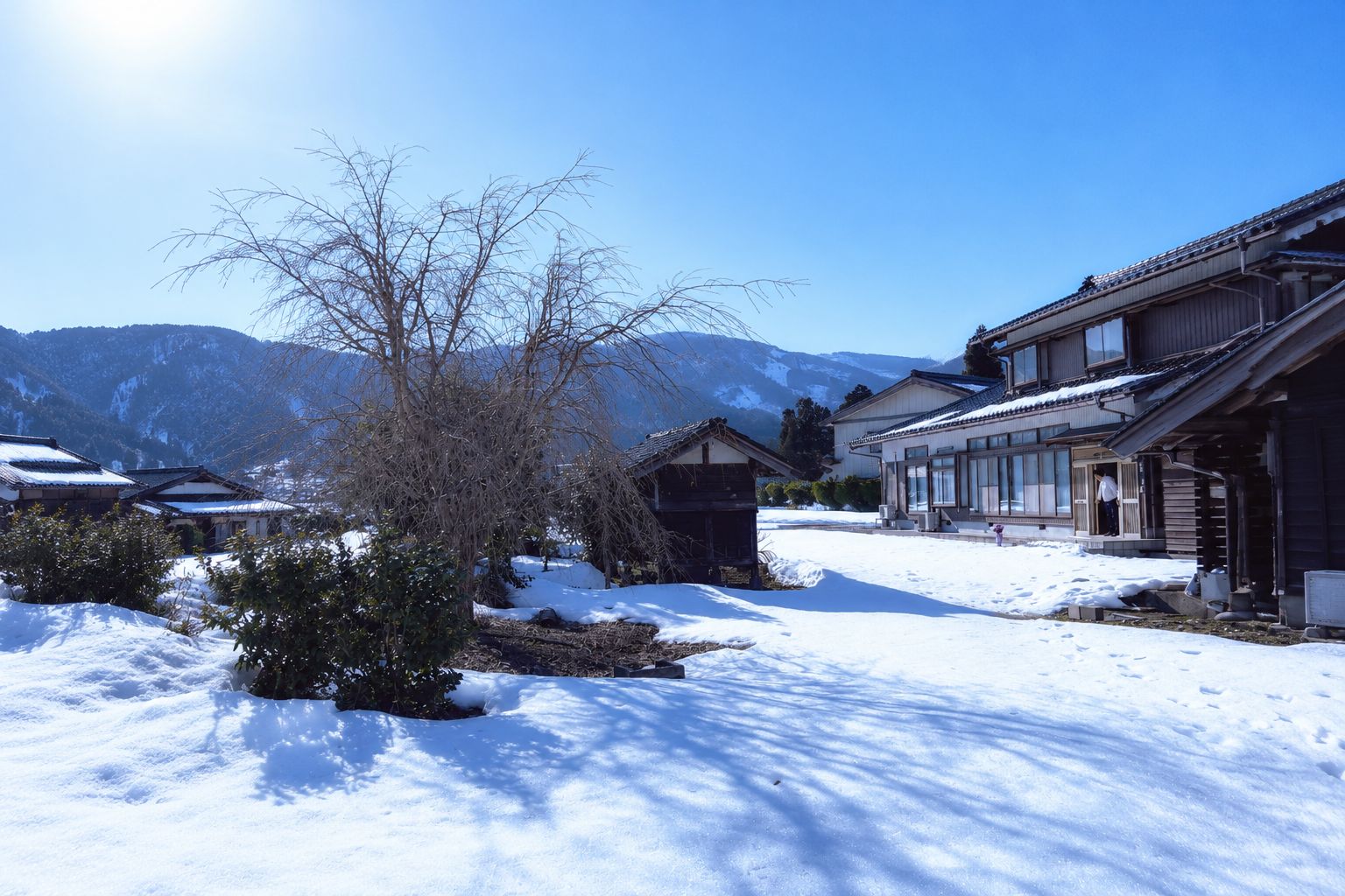 A traditional Japanese building with a snow-covered landscape and mountains in the background.