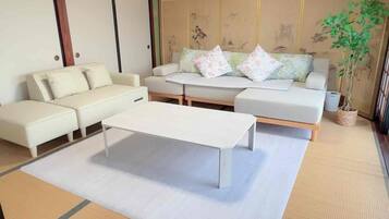 A traditional Japanese-style room with tatami flooring, a low wooden ceiling, and a central tatami mat table.