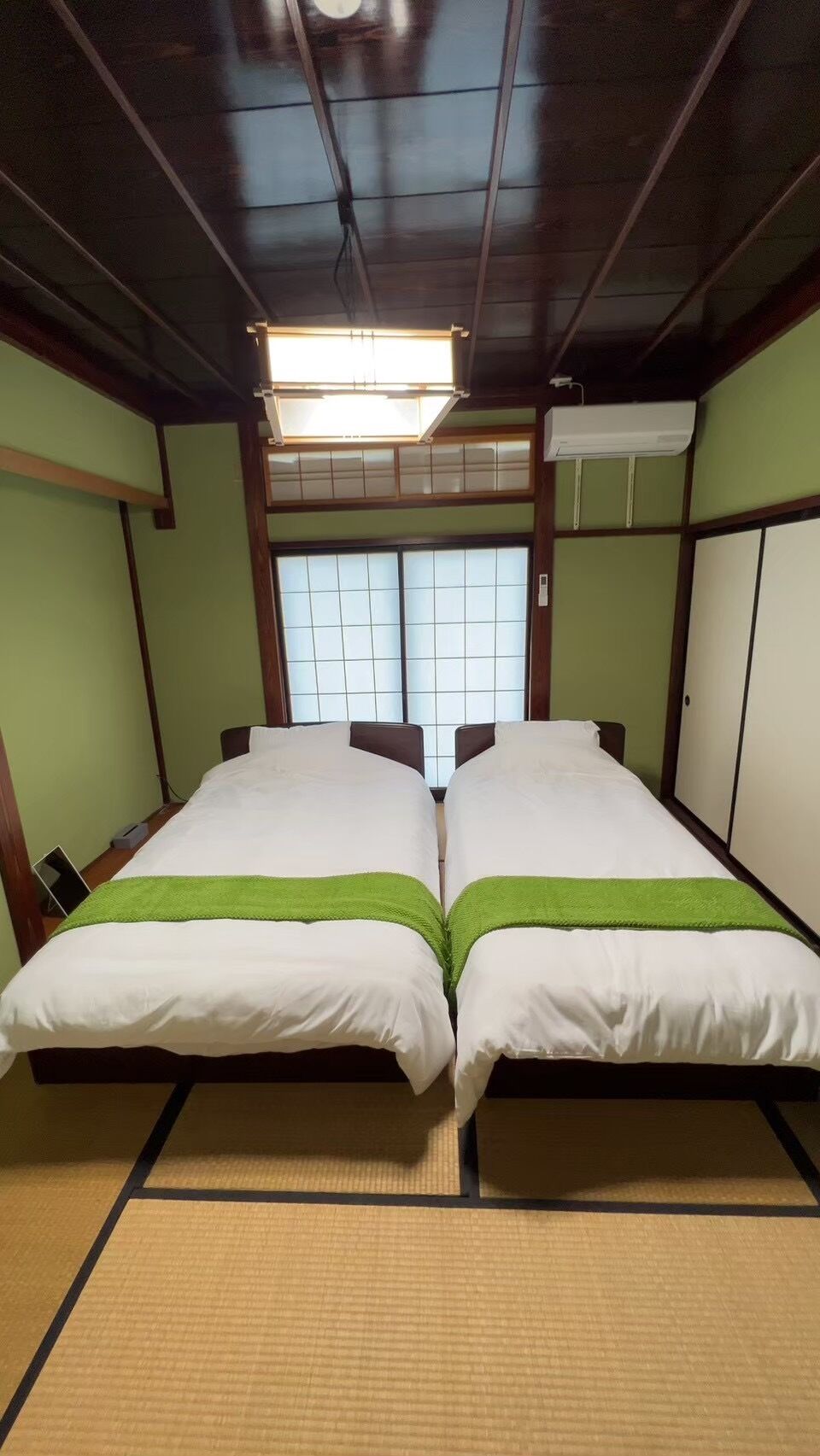 A room with two beds, a window with a view, a ceiling fan, and a wall-mounted air conditioner.