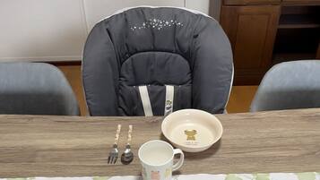 Un comedor con una trona, una mesa con mantel floral y un armario al fondo.