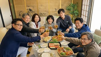 Un grupo de personas sentadas alrededor de una mesa con comida y bebidas, en una habitación con decoración tradicional.