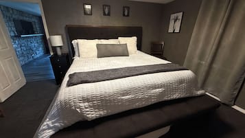 Una habitación de hotel con una cama grande, una mesita de noche, una lámpara, una silla y vistas a un muro de piedra y una puerta que da a otra habitación.