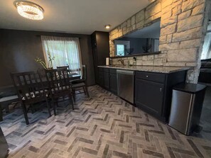 A kitchen with a stone wall, a dining table with chairs, and a herringbone floor pattern. - Modern Retreat / Office / Deck / Massage Chair (Independence)