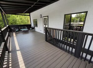 A covered outdoor deck with wooden flooring, black railings, and seating furniture. - KC Group Getaway - Spacious, Very Private - 14+ Ppl - Perfect for Chiefs games! (Independence)