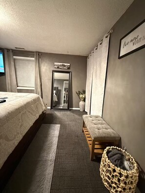 Een hotelkamer met een bed, een bankje, een klein tafeltje, een spiegel aan de muur en een lijst met een bordje.