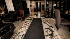 Ein Zimmer mit einer schwarzen Ledersofa, einem Holzstuhl, einem schwarzen Teppich und einem Regal mit dekorativen Gegenständen.