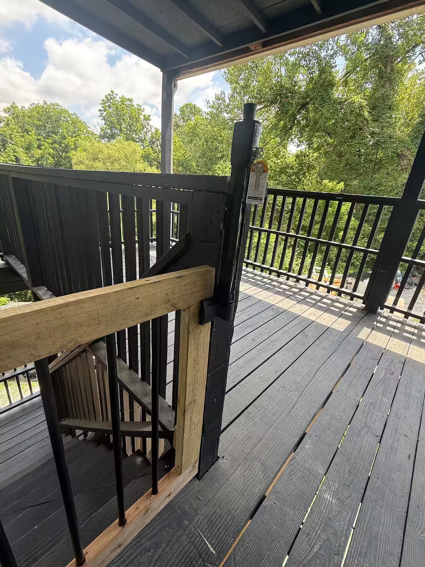 A wooden deck with a railing, a metal post, and a wooden handrail.
