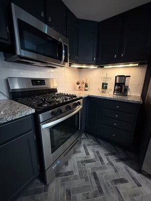 A modern kitchen with stainless steel appliances, dark cabinetry, and a herringbone tile floor. - KC Group Getaway - Spacious, Very Private - 14+ Ppl - Perfect for Chiefs games! (Independence)