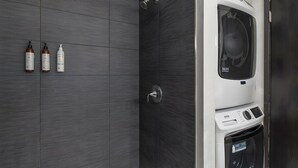 Uma casa de banho moderna com azulejos cinzentos, um chuveiro e uma máquina de lavar integrada.