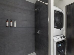 A modern bathroom with grey tiles, a shower, and a built-in washing machine. - 4BR for 12, 2 Condos - Hale Kamaole, Kihei! (Kihei)