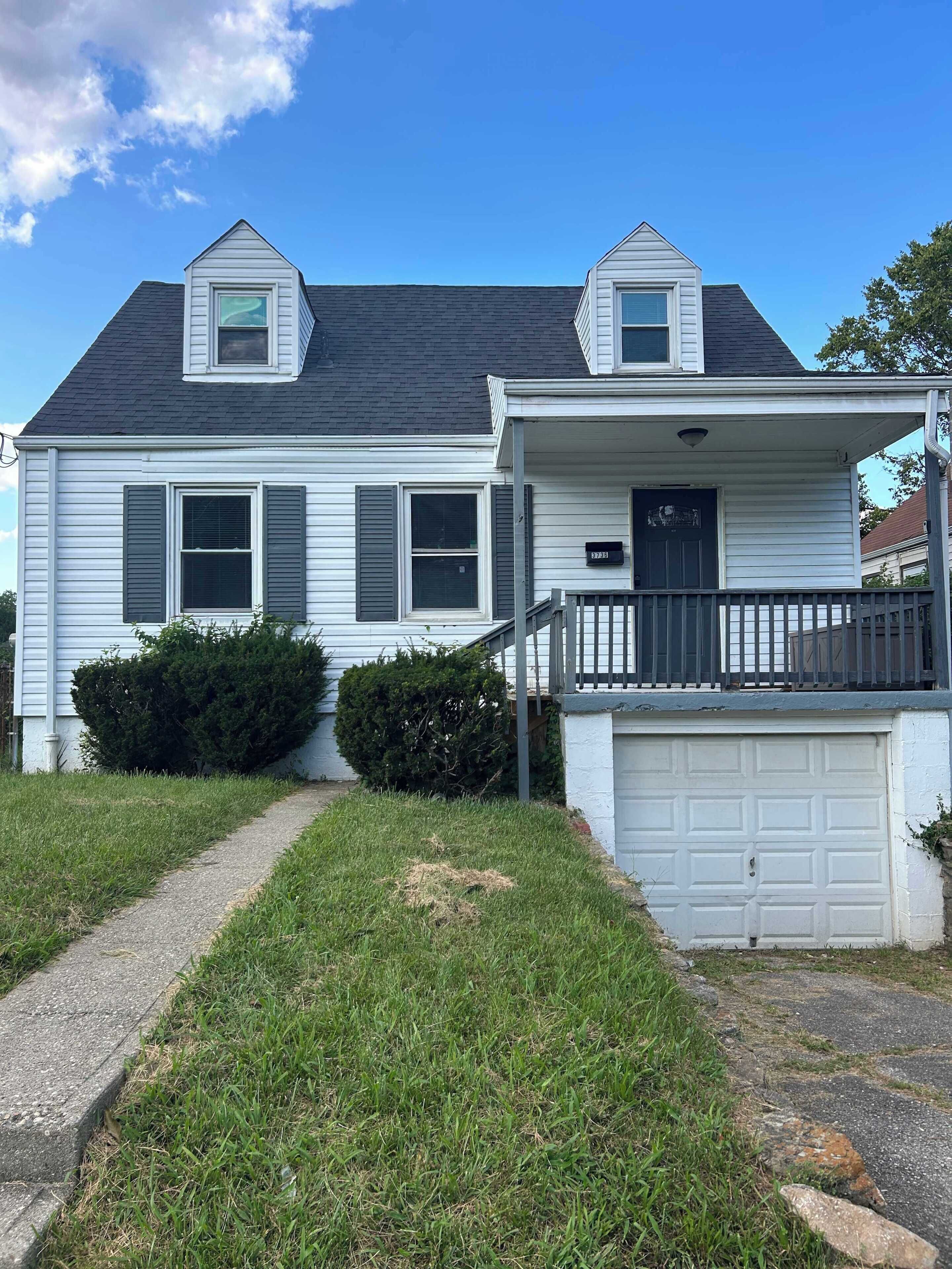 A two-story house with a front porch, a garage, and a pathway leading to the entrance.