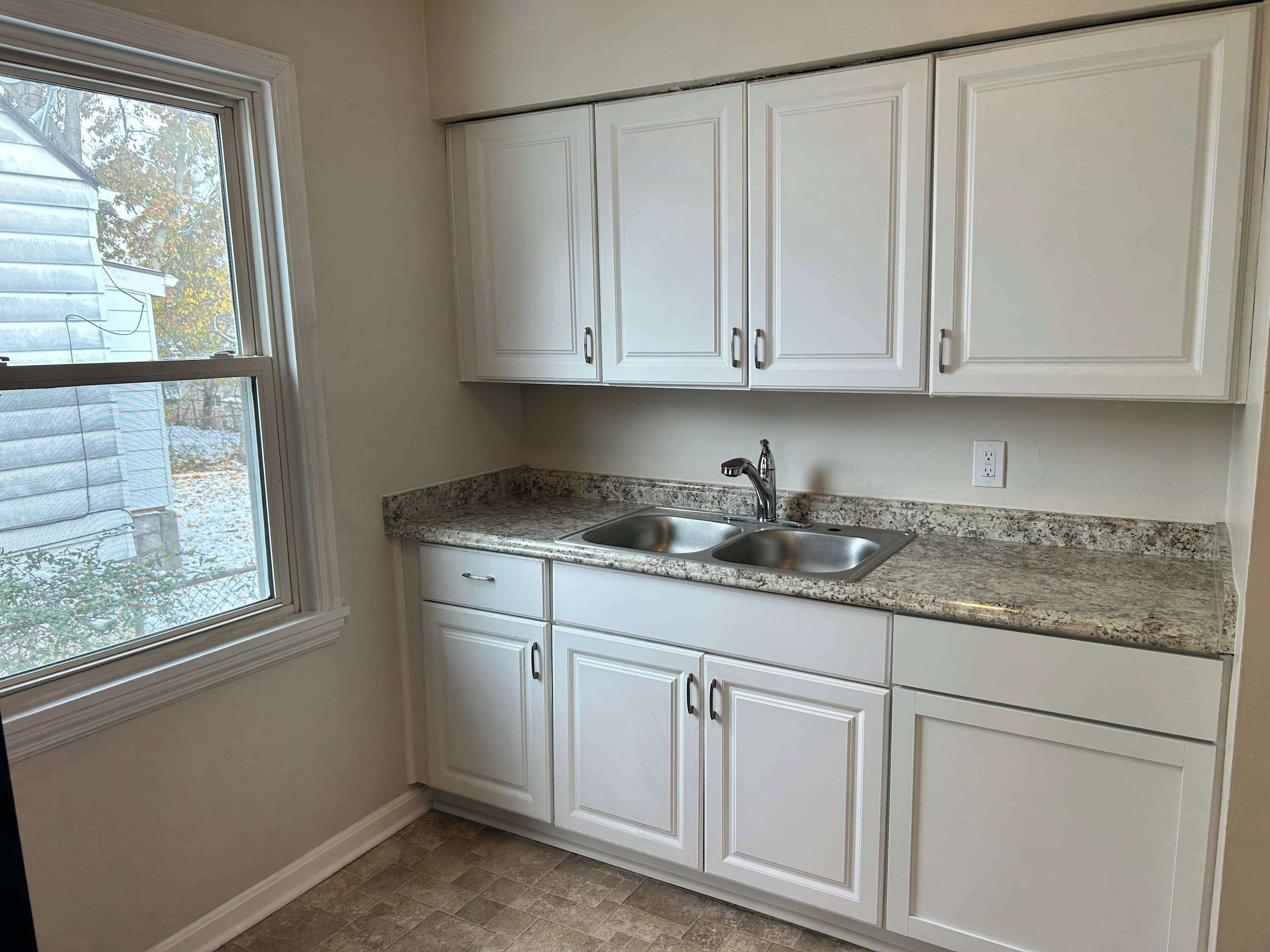 A kitchen with white cabinets, a granite countertop, and a window.