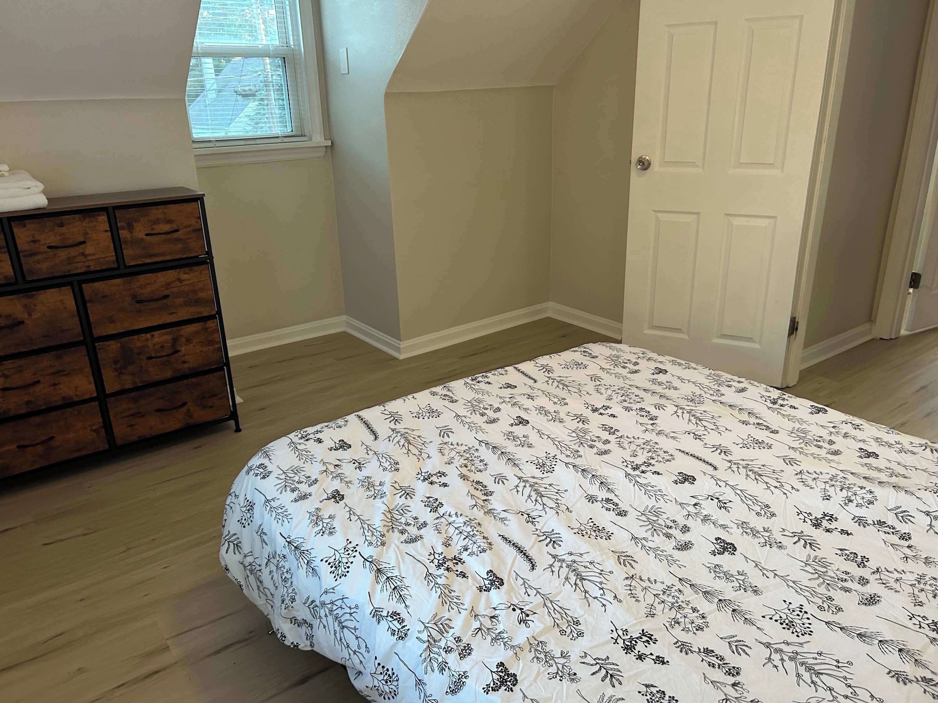 A bedroom with a bed, a dresser, a window, and a door.