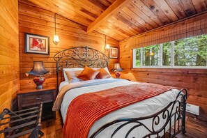 Ein Schlafzimmer einer Holzhütte mit einem Bett, zwei Nachttischen und einem Fenster.