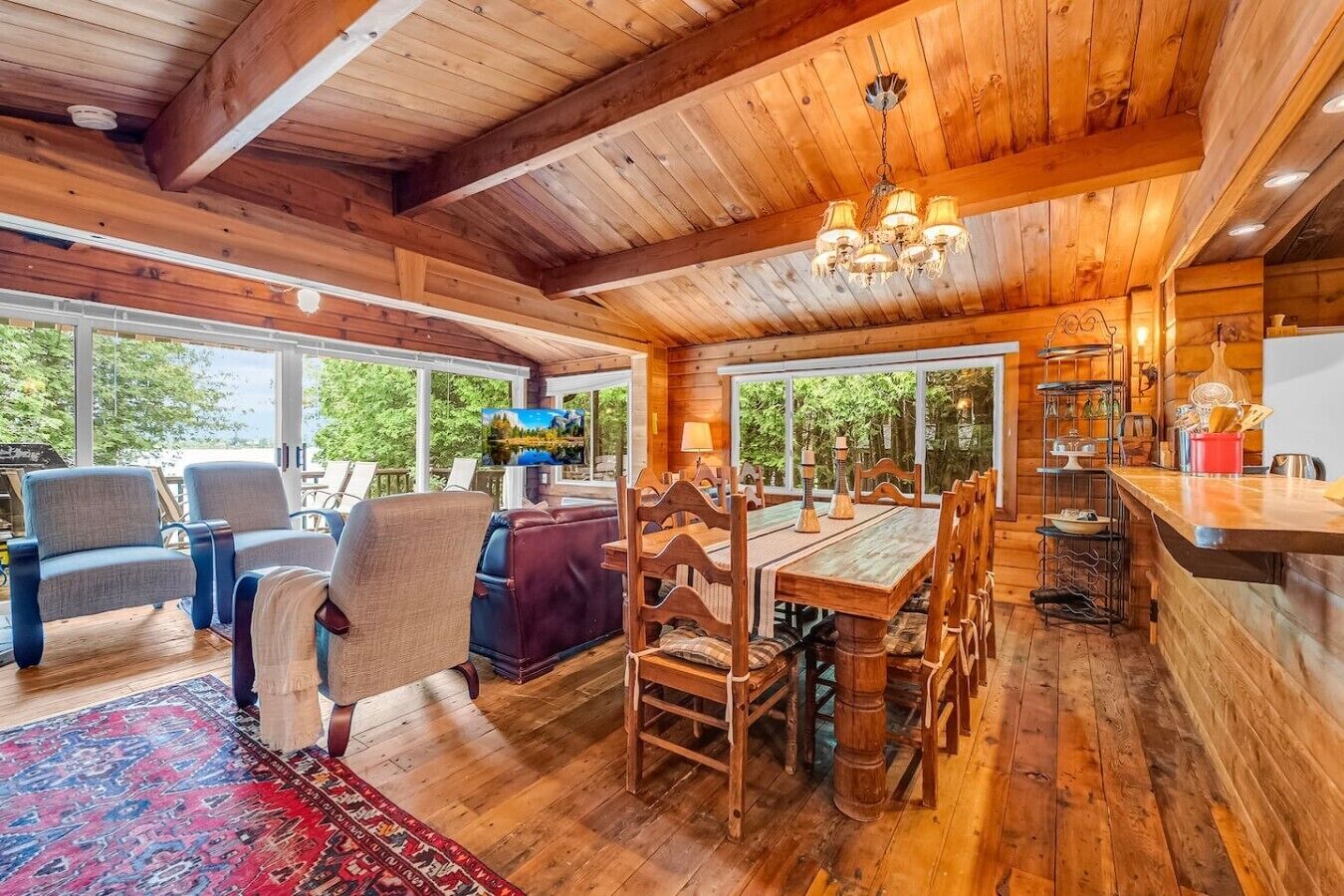 Un interior de madera con comedor, sillas, una mesa y vistas amplias por ventanas grandes.