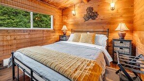 Camera da letto in una baita di legno con un letto, due lampade da comodino, una finestra e un lampadario a parete.