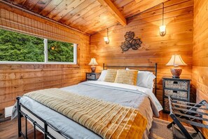 Ein Schlafzimmer einer Holzhütte mit einem Bett, zwei Nachttischlampen, einem Fenster und einer Wandleuchte.
