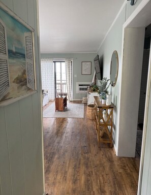 A hallway with wooden flooring, a wooden bench, a wall-mounted mirror, and a framed picture. - Marnier’s Cove Condo unit 301 A Myrtle Beach (Myrtle Beach)