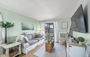 A cozy living room with a sofa, a small table, a plant, and a view of the outdoors through a glass door. - Marnier’s Cove Condo unit 301 A Myrtle Beach (Myrtle Beach)