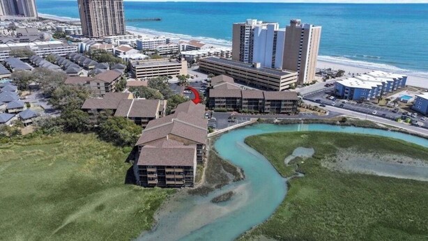 Een kustgebied met woningen, een kronkelend waterpartij en een strand op de achtergrond.