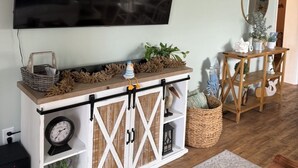 Een woonkamer met een wandtelevisie, een houten console en decoratieve objecten, een klein horloge en een plant.