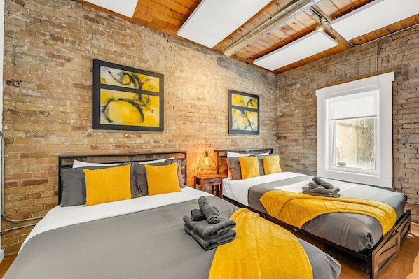 A hotel room with two beds, a brick wall, and artwork.