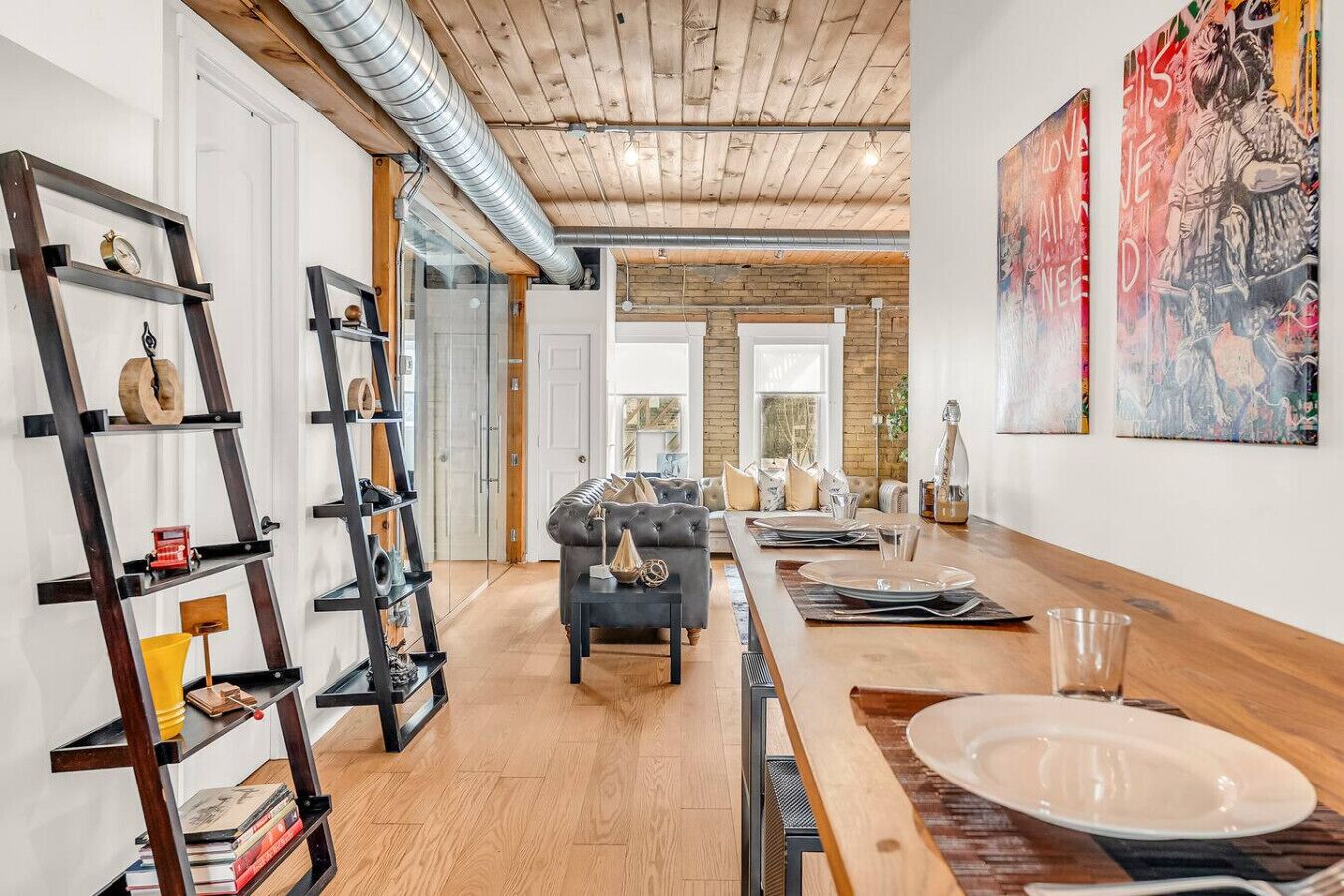 A modern living room with a wooden ceiling, a sofa, a dining table set, and artwork on the walls.