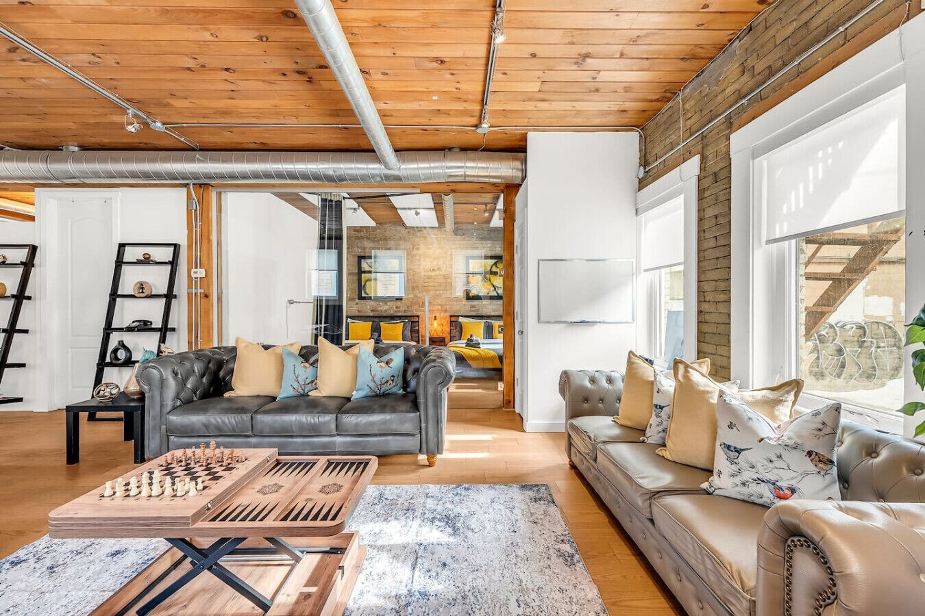 A spacious living room with a wooden ceiling, a fireplace, a sofa, a coffee table, and a chessboard.