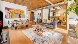 A spacious living room with a wooden ceiling, a large abstract painting, a sofa, a coffee table, and a dining area with chairs and a table.