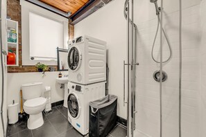 A compact laundry room with stacked washers and dryers, a toilet, and a shower. - *Golden Loft*- RARE Downtown 2BR + Parking & Games (Toronto)