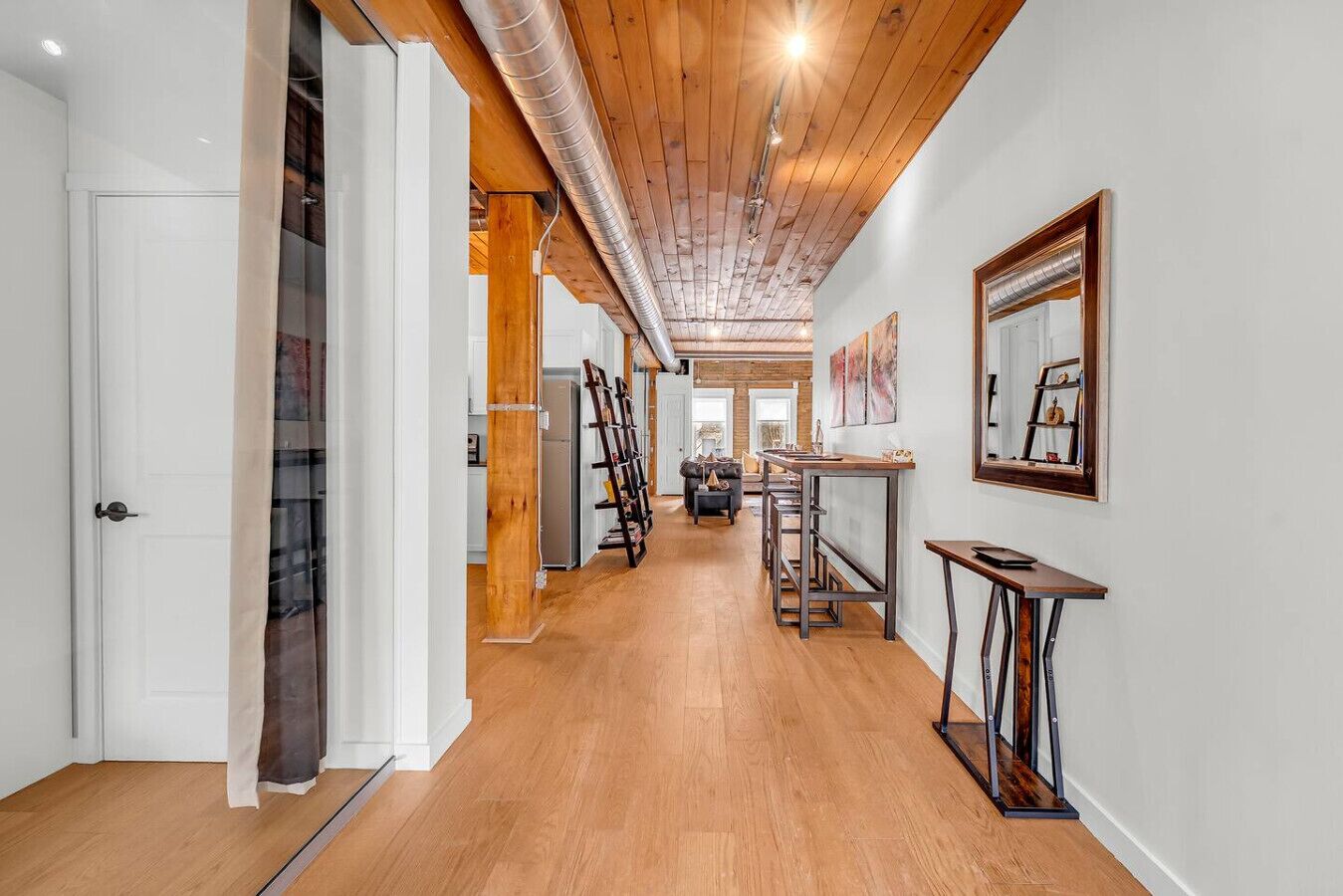 A hallway with wooden flooring, a white door, and a staircase with a glass railing.