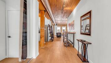 A hallway with wooden flooring, a white door, and a staircase with a glass railing.