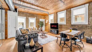 A modern living room with a sofa, dining table, and chairs, a television, and a brick wall.