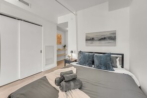 A bedroom with a bed, a nightstand, a lamp, a painting, and a closet. - *World Cup* Stylish Downtown Apartment With Gym (Toronto)