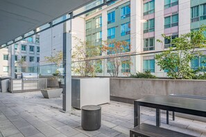 Eine Außenpatio-Terrasse mit Grill, Sitzgelegenheiten und Blick auf moderne Gebäude.