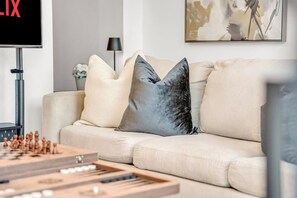 Ein Wohnzimmer mit einem beigefarbenen Sofa, zwei Kissen, einem Fernseher und einem Schachbrett.