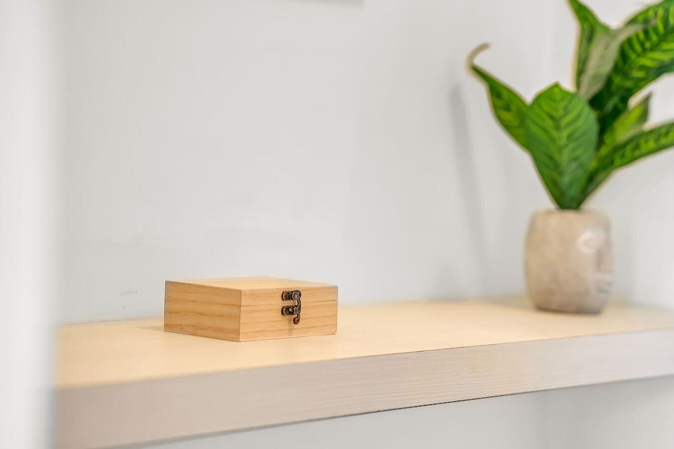 Een houten doos met een metalen sluiting op een wit plank.