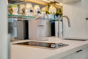 Una cocina moderna con cafetera integrada, un lavamanos de acero inoxidable y frascos decorativos en un estante de vidrio.