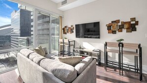 A modern living room with a large window, a sofa, a TV, and a unique wall art piece. - *In the Heart* Spacious Condo Right in Downtown (Toronto)