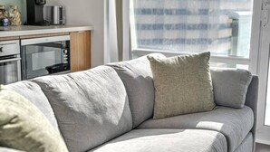 A modern living room with a grey sofa, a coffee machine, and a window with blinds. - *In the Heart* Spacious Condo Right in Downtown (Toronto)