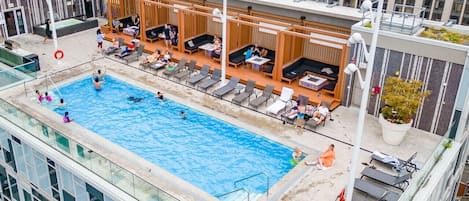 Un área de piscina en la azotea con mobiliario de salón y vistas del paisaje urbano.