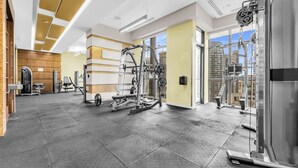 A gym with various exercise equipment, a clear exit sign, and a view of the city through large windows. - *In the Heart* Spacious Condo Right in Downtown (Toronto)