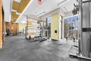 Ein Fitnessraum mit unterschiedlichen Trainingsgeräten, einem gut sichtbaren Fluchtweg und Blick auf die Stadt durch große Fenster.