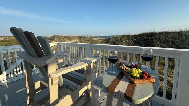 A deck with a table set for two, featuring a fruit platter and two glasses of red wine. - Peak-A-Blue: Beautifully Renovated Oceanfront Home with Hot Tub (Oak Island)