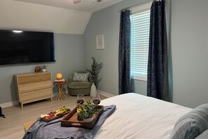 Ein Schlafzimmer mit einem Bett, einem Fernseher, einem kleinen Nachttisch, einem Stuhl und einem Fenster mit Vorhängen.