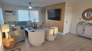 A living room with a sofa, coffee table, and a television mounted on a wooden wall. - Peak-A-Blue: Beautifully Renovated Oceanfront Home with Hot Tub (Oak Island)