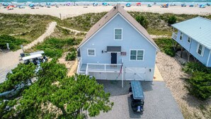 A two-story house with a front porch, a garage, and a view of the beach. - Peak-A-Blue: Beautifully Renovated Oceanfront Home with Hot Tub (Oak Island)