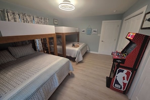 Ein Zimmer mit Etagenbetten, einem kleinen Tisch mit Flaschen, einem an der Wand befestigten Aquarium und einem NBA-Arcade-Spiel.
